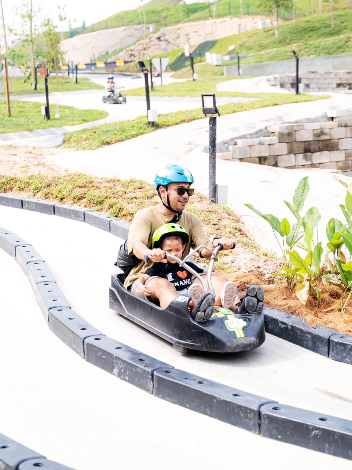 A father finishes a Luge ride with his son in the same cart.