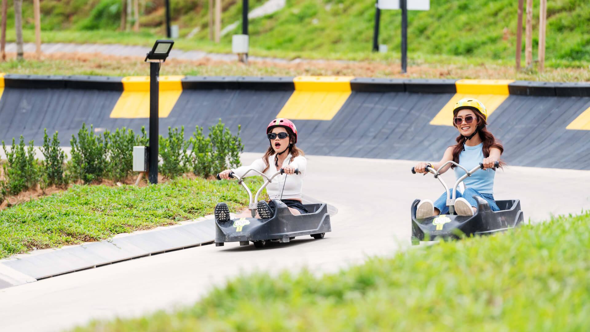 Two friends Luge down the tracks next to each other smiling and screaming with excitement.
