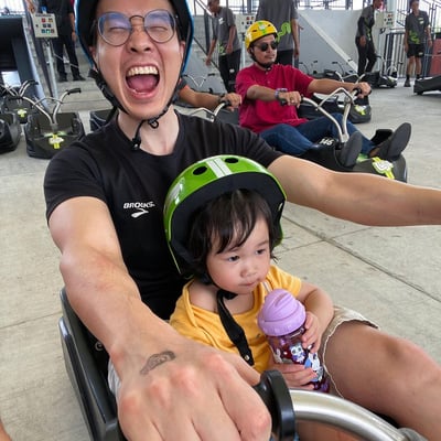 A father smiles in excitement ready to go Luging with his daughter in the same cart.
