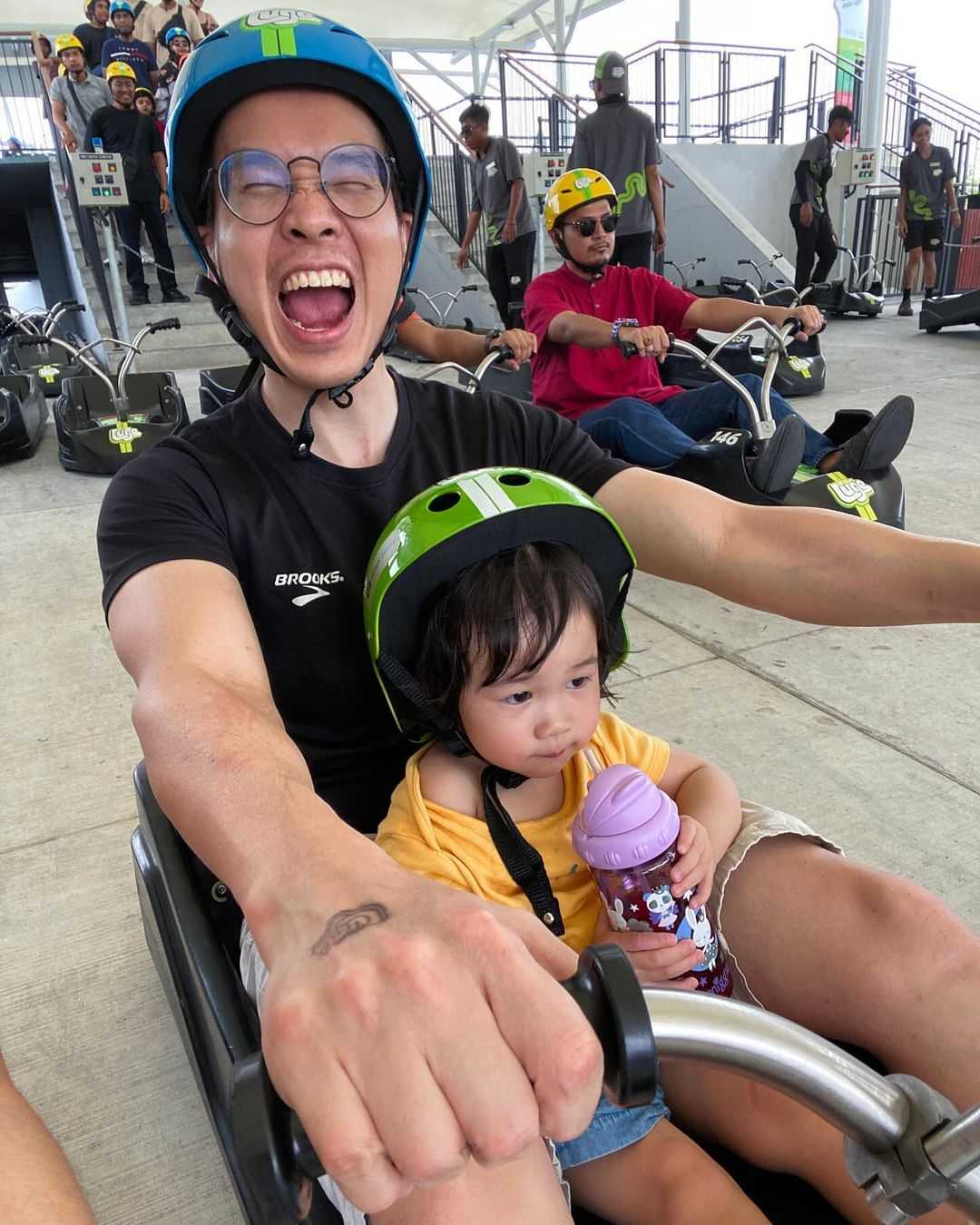 A father smiles in excitement ready to go Luging with his daughter in the same cart.
